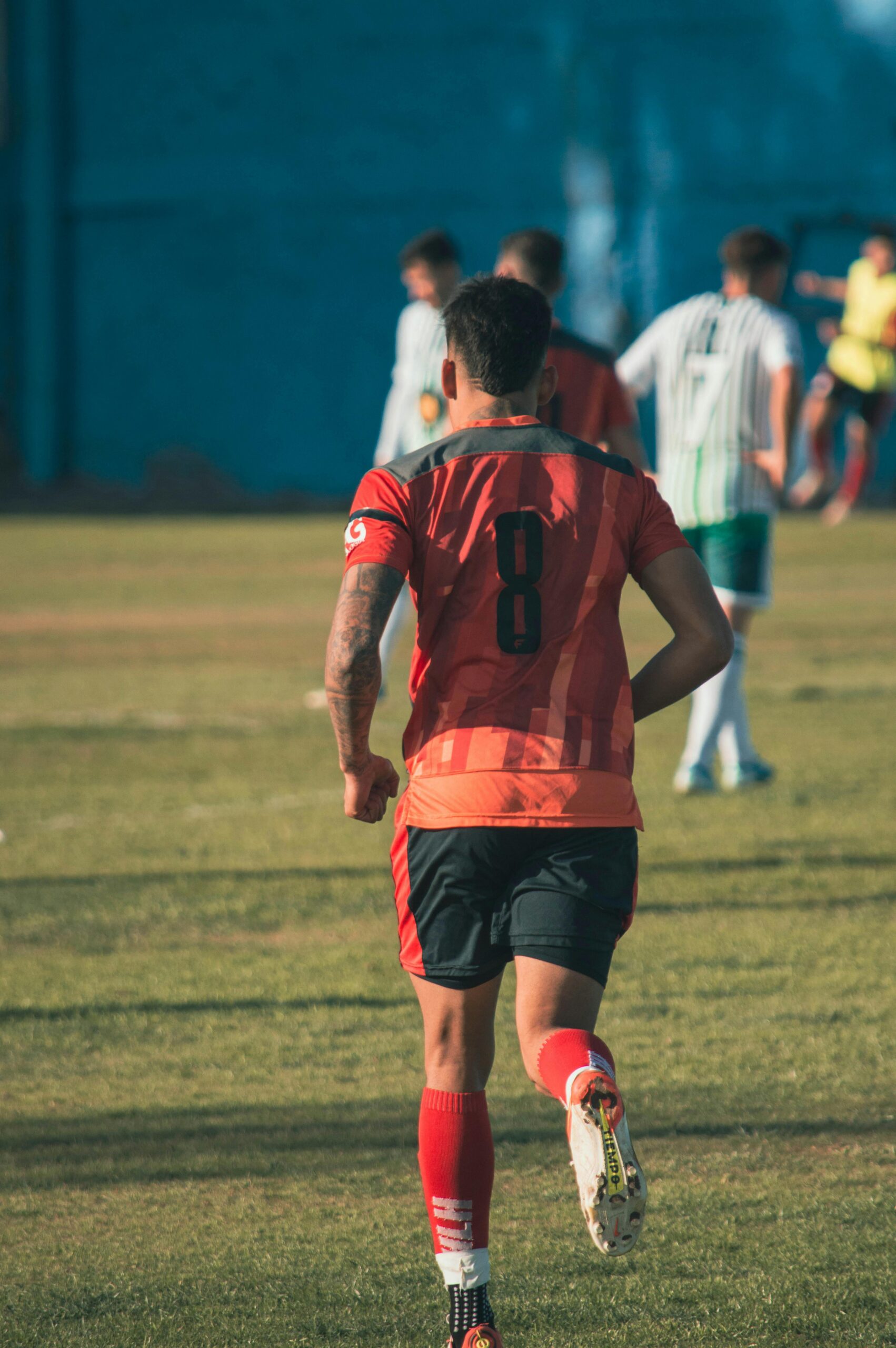 Soccer player wearing jersey number 8 running on a grass field during a game in daylight.