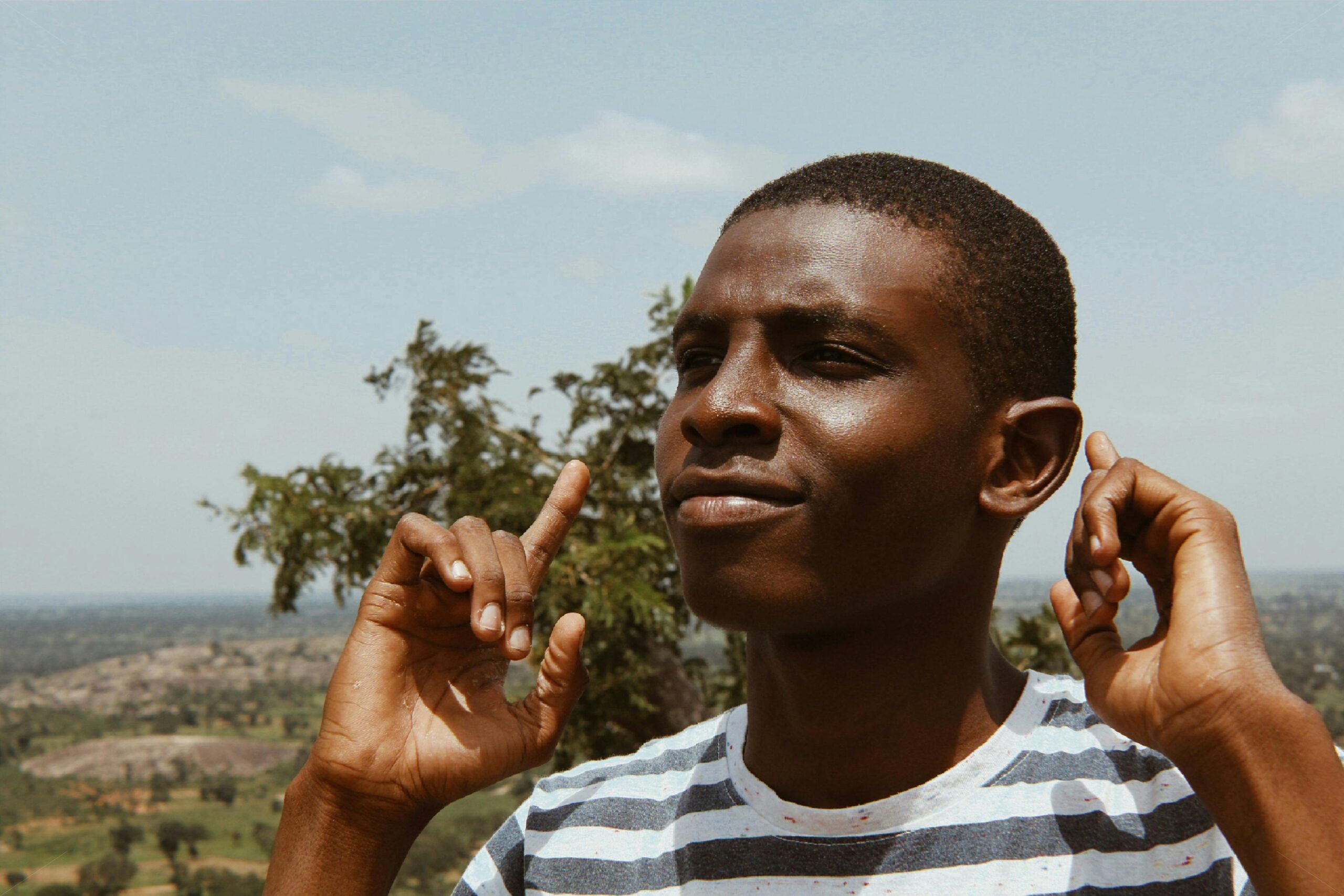 A young black man smiling and posing outdoors on a sunny day.